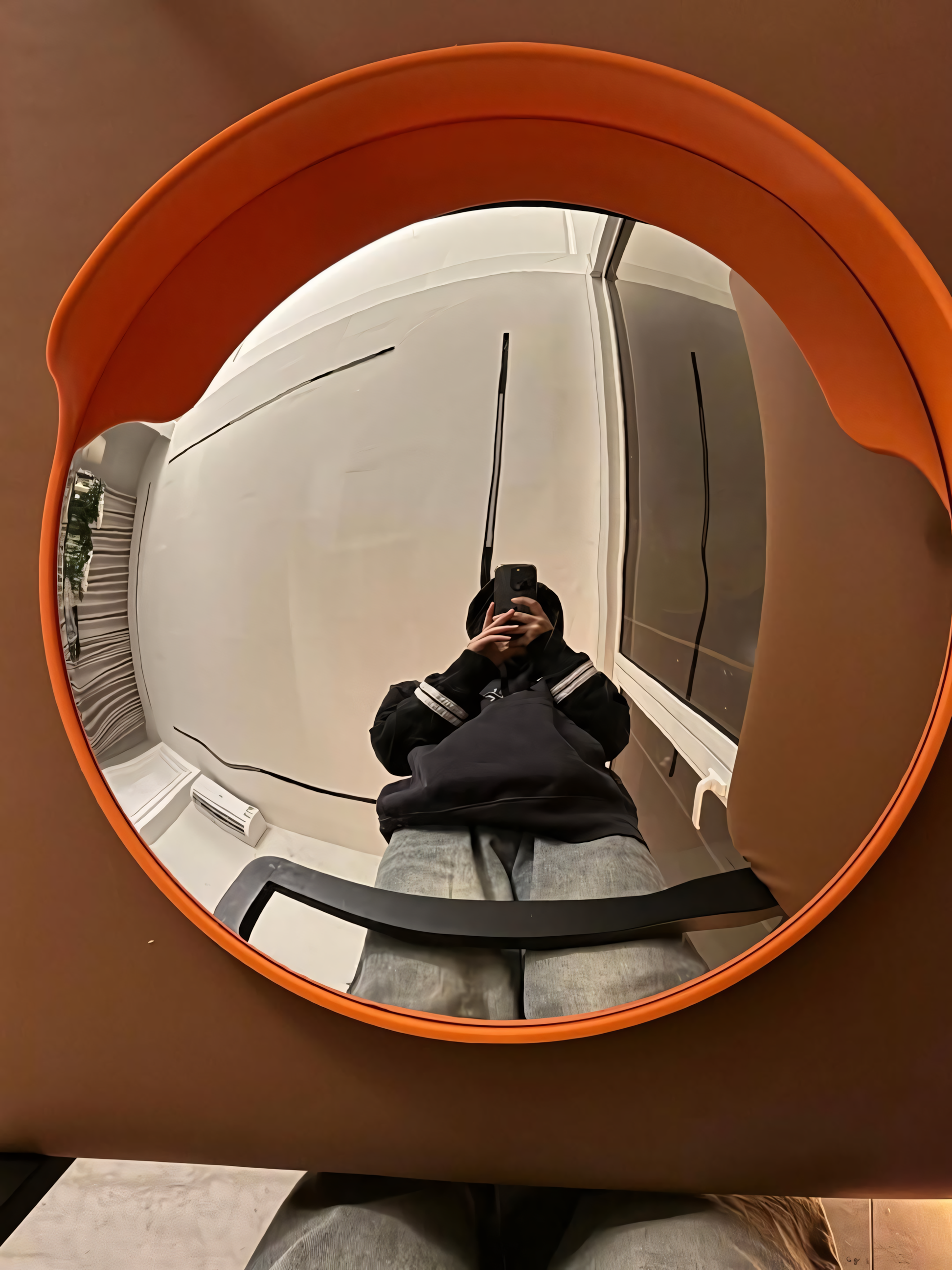 Person taking a mirror selfie with an orange-framed convex mirror.